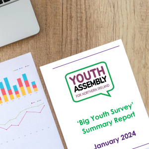 A desk with the edge of a laptop in view in the top left corner. On the desk are two pages of a report. One page shows random graphs and tables. The other page is the title page of the Youth Assembly's 'Big Youth Survey' report.