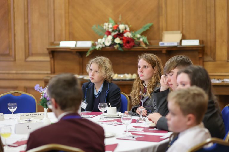 Youth Assembly Members sitting at a white round table with information packs on the table in front of them